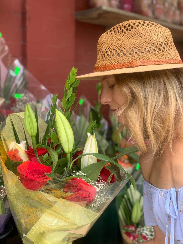 A blond and young woman with a straw hat smelling a bouquet of flowers in the summer in New York. 