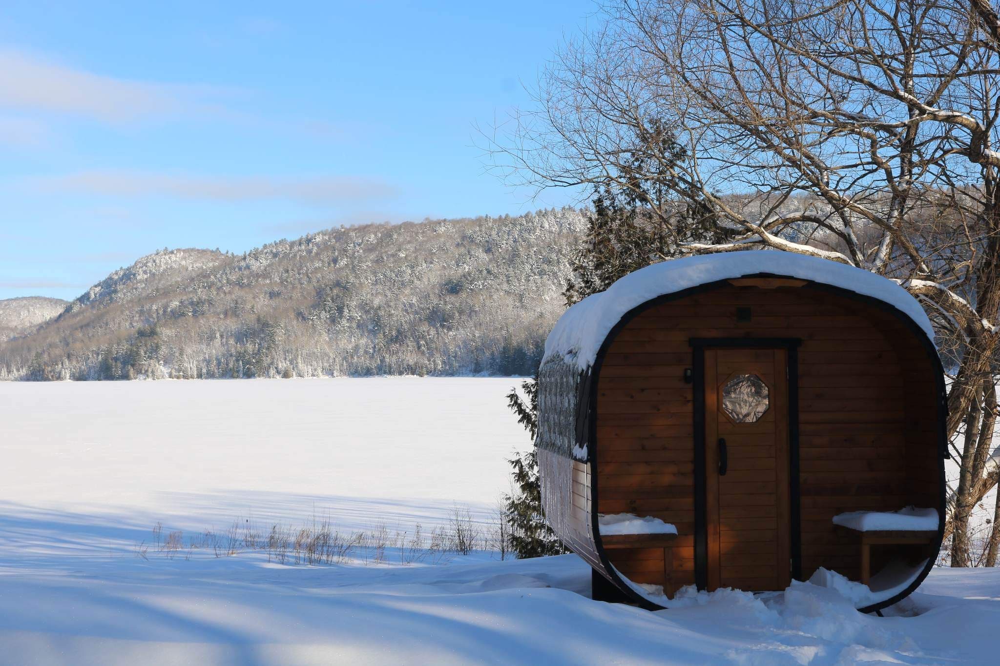 A sauna cabin in the snowy landscape with an iced lake behind in Quebec, Canada.