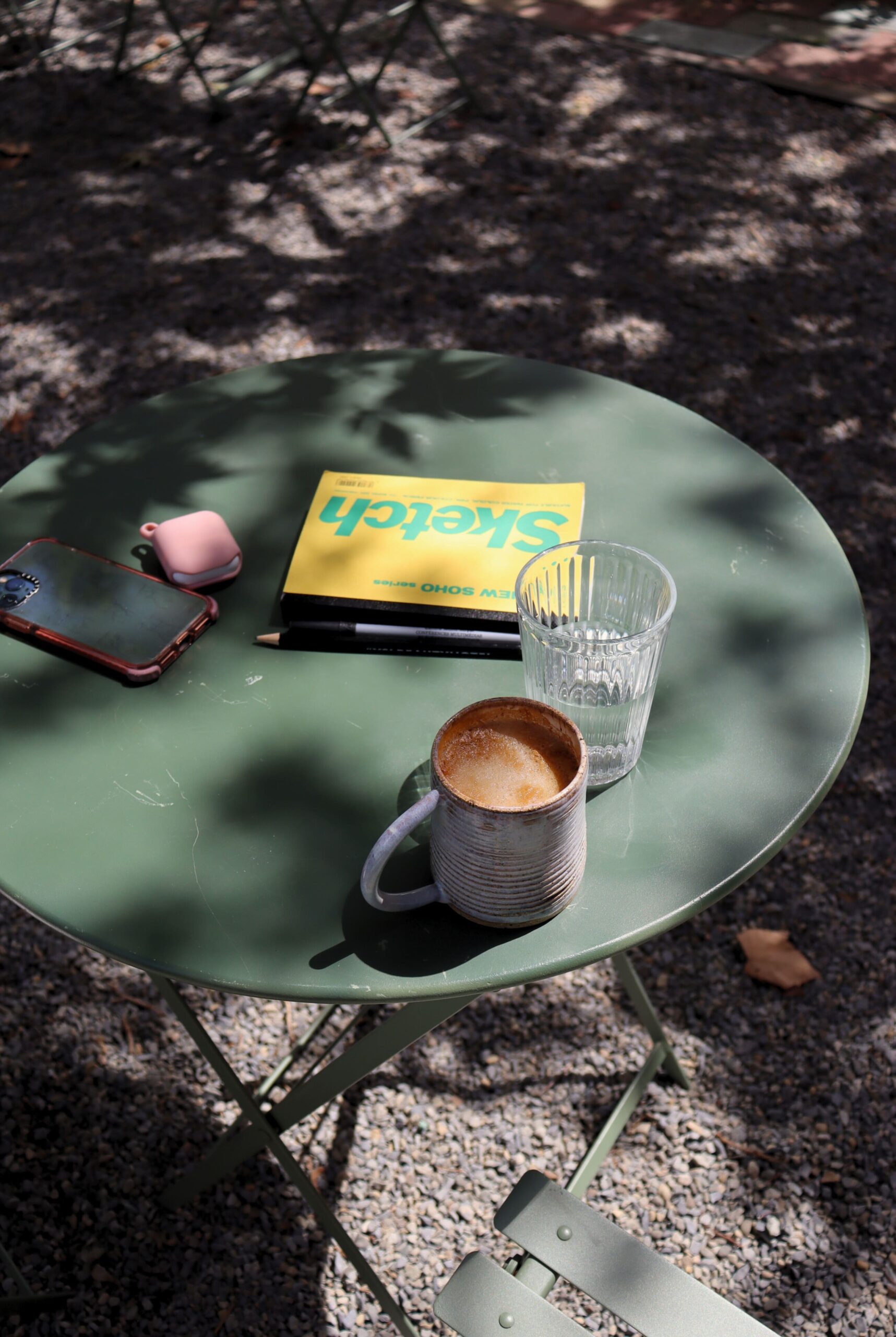 A table in the shade with a coffee and a sketch book in Brooklyn, New York.